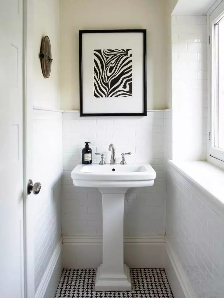 Small eclectic bathroom featuring framed abstract art in a black and white palette hanging above a white pedestal sink, adding personality and style to the white tile and black and white patterned room.