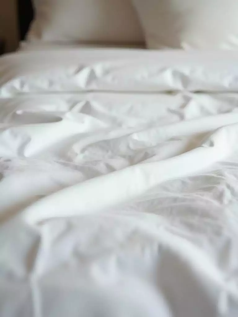 A detailed close-up of luxurious white sateen sheets on a bed, showcasing their smooth texture and subtle sheen in natural light.