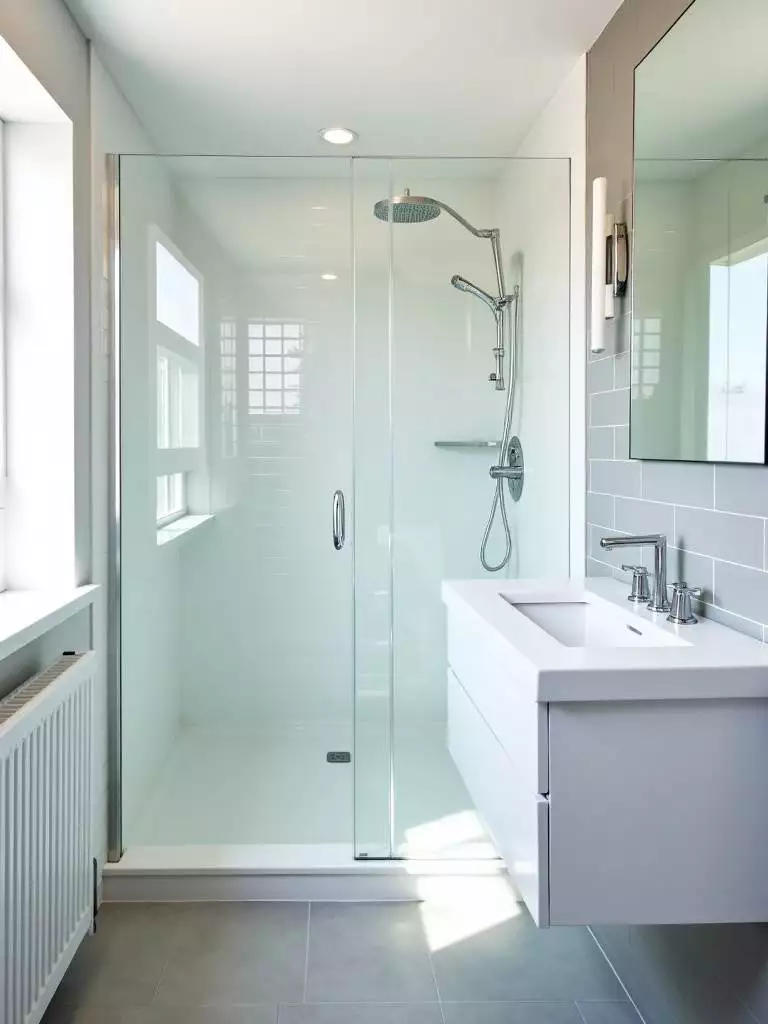 Small contemporary bathroom with a clear glass shower enclosure in the corner, maximizing visual space and light flow, complemented by white subway tiles and a floating vanity.