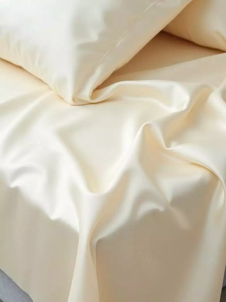 Close-up of cream-colored silk sheets highlighting their smooth texture.
