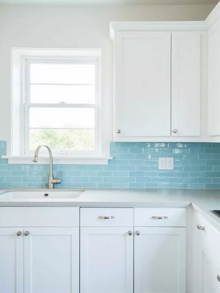 Light blue glass tile backsplash in a bright, modern kitchen, reflecting natural light.