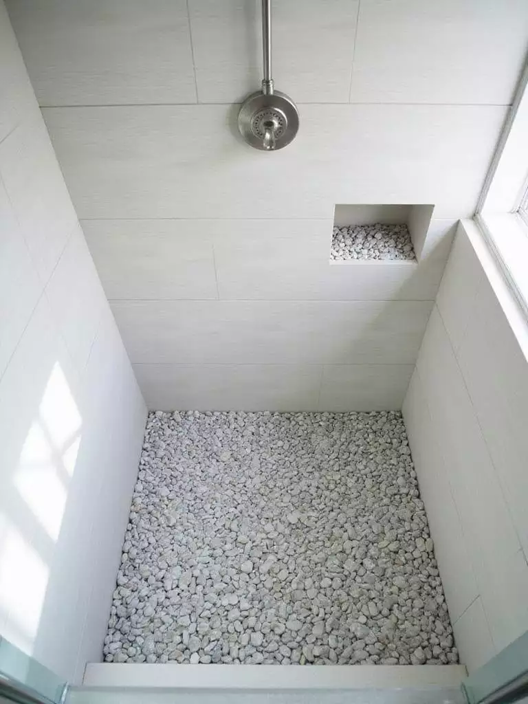 Coastal bathroom shower floor covered in smooth river pebbles.