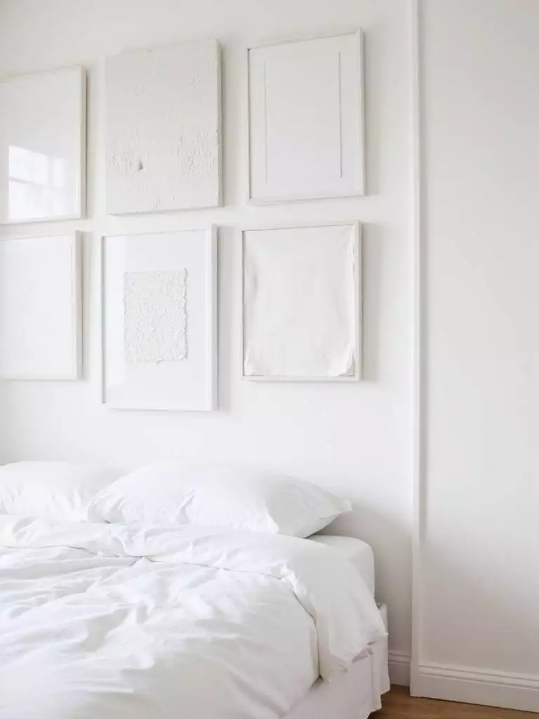 Serene white bedroom with a monochromatic white art gallery wall above the bed.