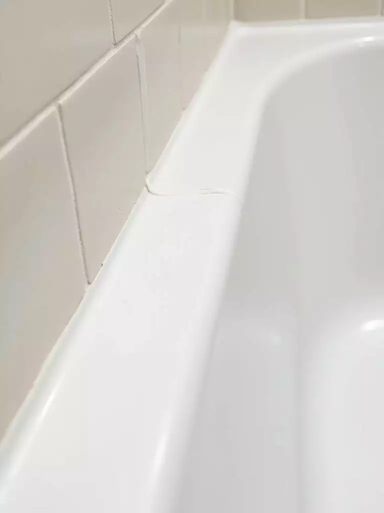 New, clean white caulk sealing the gap between a bathtub and tiled bathroom wall.