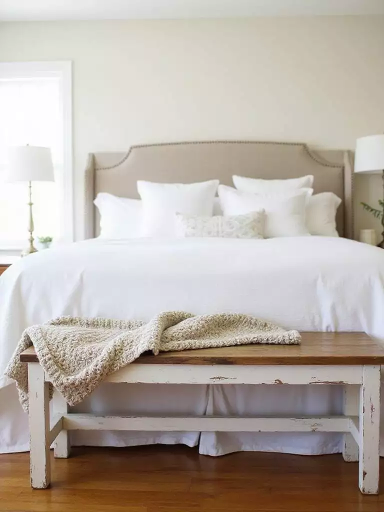 Farmhouse bedroom with white linen bedding and a rustic wooden bench at the foot of the bed.