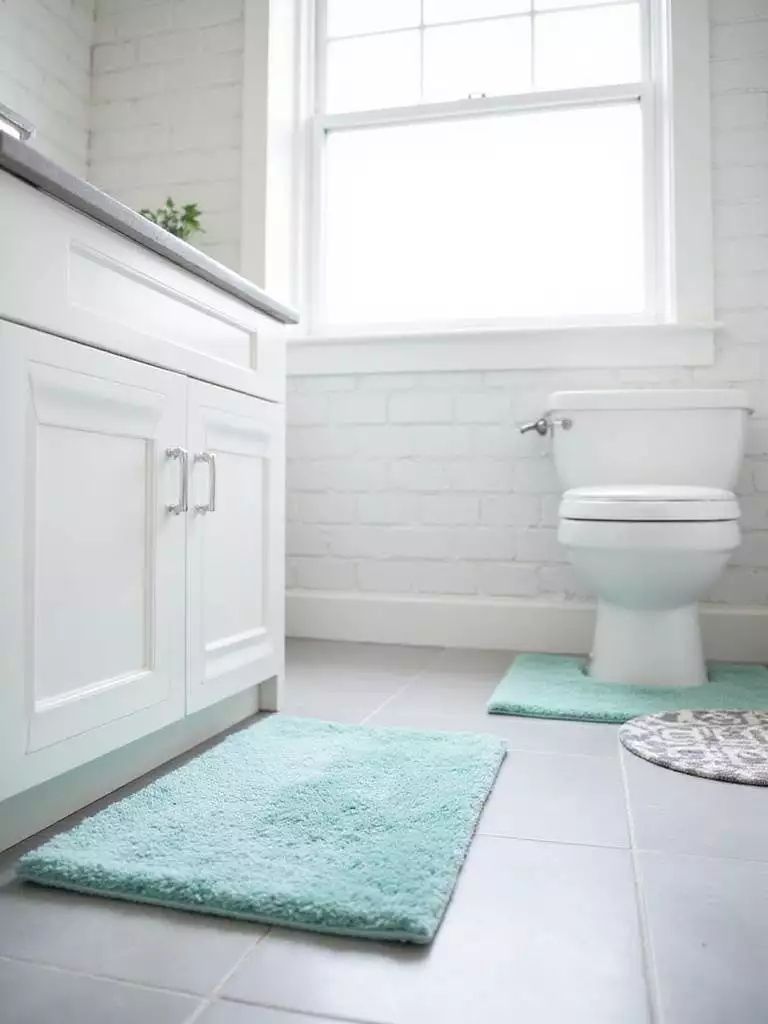Bathroom floor featuring a teal bath mat in front of the vanity and a grey and white patterned rug next to the toilet.