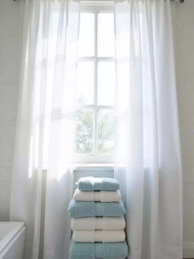 Coastal bathroom with linen curtains and blue and white cotton towels.