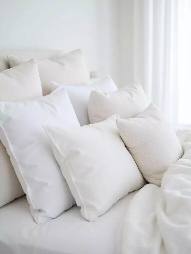 Serene white bedroom with layered white decorative pillows on the bed