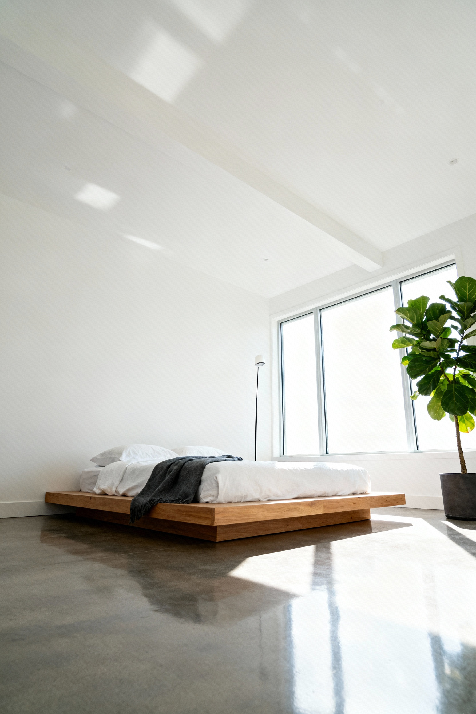 A spacious, minimalist bedroom featuring a low-profile natural oak platform bed that grounds the floor space, enhancing the illusion of high ceilings and breathable decor.