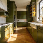 High-end kitchen featuring deep olive green cabinets and white marble island with warm natural lighting.