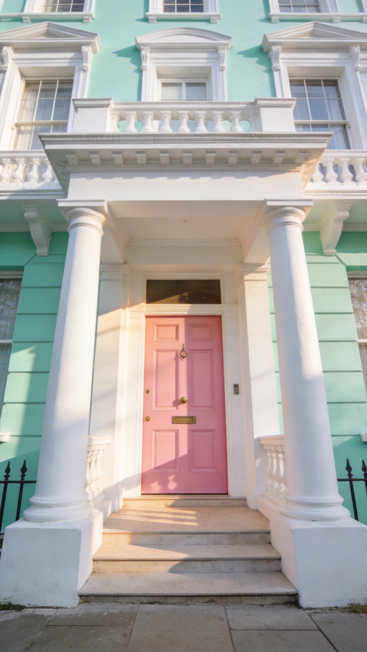 A Notting Hill style porch featuring a blush pink door and mint green accents framed by thick white stucco pillars.